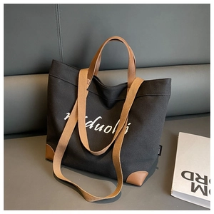 Detail of black canvas tote bag with brown leather corners on a dark gray leather sofa