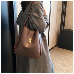 Detail view of brown leather bucket bag with gold square buckle worn by a model