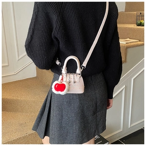 Pink polka dot shell crossbody bag featuring a plush cherry charm and sleek top handle