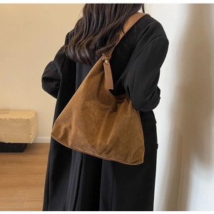 Close-up of caramel suede hobo bag worn by a person in a black coat for a minimal look
