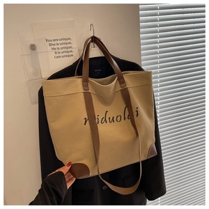 Detail of khaki canvas tote bag with brown leather trim and artistic letter print