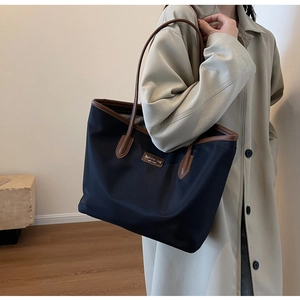 Detail der wasserdichten schwarzen Nylon-Tote mit braunen Griffen und Metallplakette