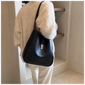 Detail of a minimalist black leather hobo bag with elegant gold clasp on a female model