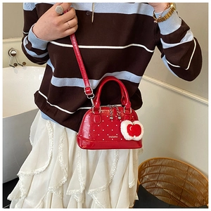 Close-up of red polka dot shell bag with heart pompom and polished faux leather finish