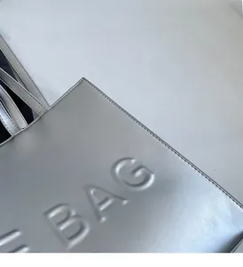 Detail of silver metallic tote bag with embossed BAG lettering and fine stitching