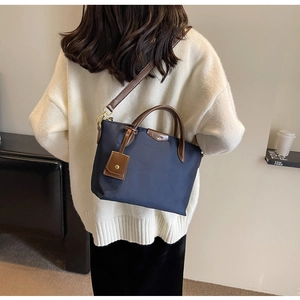 Detailed view of dark blue nylon tote bag with brown leather handles on a model back