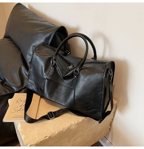 Detail of black pebbled leather travel bag with NOCO logo and adjustable shoulder strap