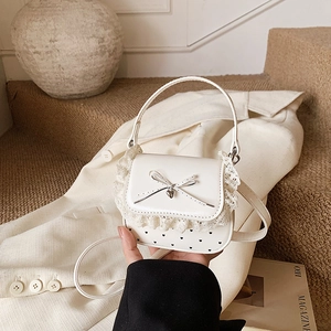 Chic white lace crossbody bag with heart dots and metal bow pendant, shown handheld