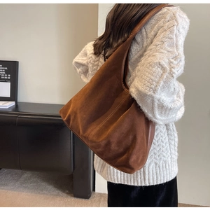 Detail of dark brown suede hobo bag with vertical stitching shown on model's shoulder