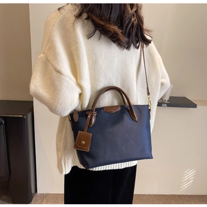 Deep blue nylon tote bag with brown leather handles and adjustable shoulder strap worn by model