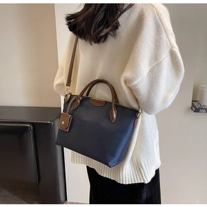 Detailed view of navy nylon tote with brown leather handles worn with a beige knit sweater