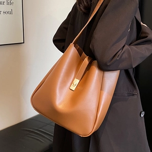 Minimalist brown leather bucket bag with gold clasp shown on a model's shoulder