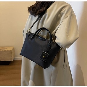 Detail of black nylon tote bag with leather trim and mini pouch on beige trench coat