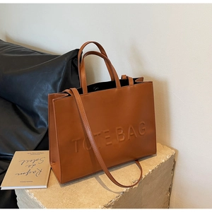 Detailed macro view of the brown leather tote bag showing the embossed TOTE BAG lettering