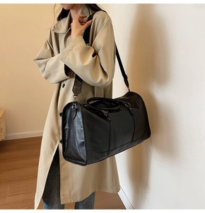 Detail of black leather travel bag showing wide shoulder strap and silver hardware