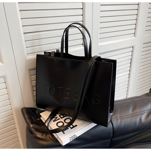 Detailed view of black leather tote bag featuring embossed TOTE BAG text and sturdy handles