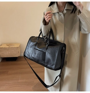 Detailed view of a large black leather travel bag with adjustable strap and silver hardware