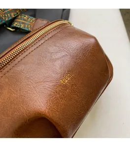 Detail of vintage brown leather chest bag with gold zipper and patterned wide strap
