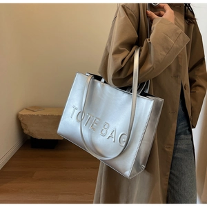 Detailed view of silver metallic tote bag with embossed lettering and slim shoulder straps