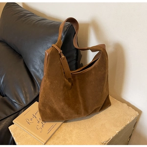 Detail view of large brown suede hobo tote bag with wide leather strap on stone stand