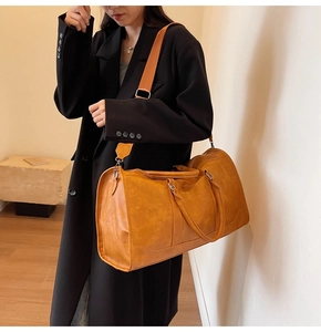 Model wearing a large ginger PU leather travel bag with adjustable strap and dual handles