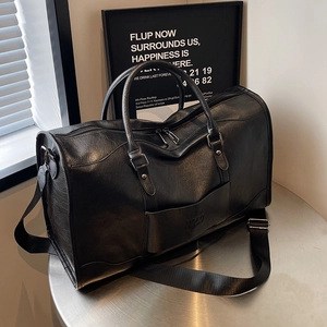 Large black faux leather travel bag with dual handles and wide shoulder strap on a metal table
