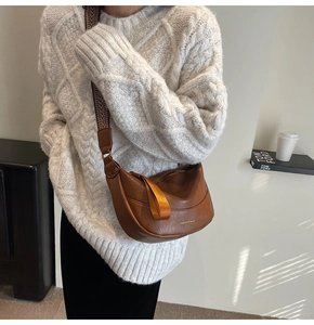 Brown leather crescent bag with geometric strap worn by model in cable knit sweater