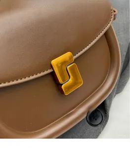 Dettaglio ravvicinato della borsa a sella in pelle marrone con chiusura geometrica dorata