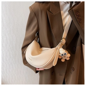 Chic beige leather half-moon bag with gold hardware and plush charm on a suit model