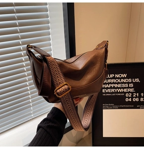 Detail of a brown leather crescent bag with a patterned woven wide shoulder strap