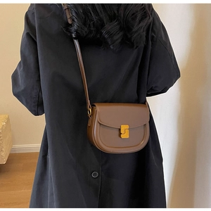 Dettaglio di borsa a sella marrone in pelle con fibbia a S dorata su un trench nero elegante