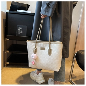 Detail view of a cream-white woven tote bag with metallic logo and cute plush charm