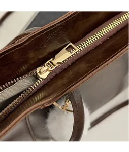 Detail of polished gold hardware zipper and soft plush charm on brown leather tote bag