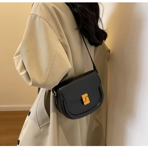 Dettaglio di una borsa a sella nera opaca con chiusura dorata su un trench beige elegante
