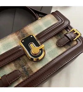 Detail of gold metal lock and brown leather trim on a green checkered handbag