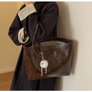 Detail of dark brown leather tote bag with a cute white plush monster keychain