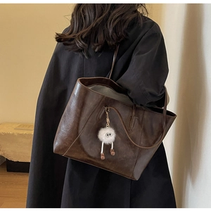 Detail of dark brown vintage faux leather tote bag with a white plush charm accessory