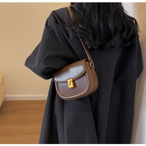 Borsa a sella in pelle marrone con fibbia dorata indossata da modella in cappotto