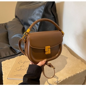 Dettaglio della borsa a sella in pelle marrone con chiusura dorata su base di pietra