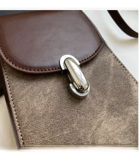Detail of a brown leather crossbody phone bag featuring a polished silver metal clasp