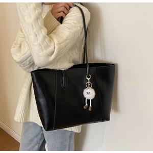 Detail of black faux leather tote bag with plush charm on beige sweater model