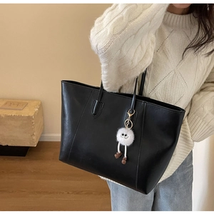 Detail of black leather tote bag with white plush monster charm on model