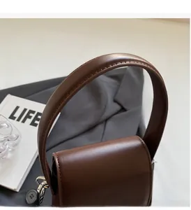 Detail view of dark brown leather handbag with rounded handle and silver hardware