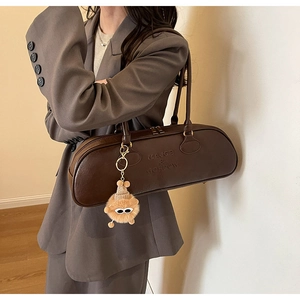 Close-up of brown cylindrical underarm bag with brand embossing and plush monster charm