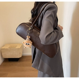 Detail view of dark brown leather shoulder bag with embossed logo and monster plush charm
