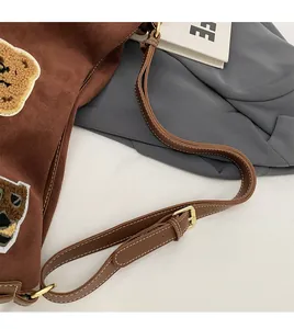 Detail view of the brown suede tote bag featuring an adjustable strap and cute bear patch