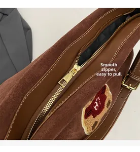 Close-up of brown suede tote bag with smooth gold zipper and bear embroidery detail