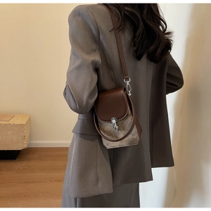 Detail of color-block crossbody bag with brown leather flap and round handle on model