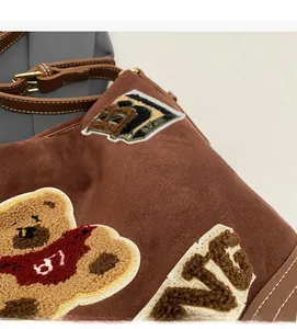Close-up of caramel brown suede tote bag with cartoon bear patches and leather handles