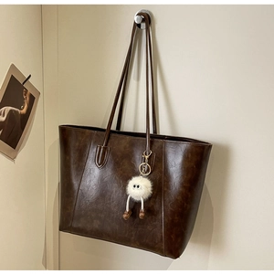 Detail of a brown leather tote bag with a white plush doll charm for a playful touch